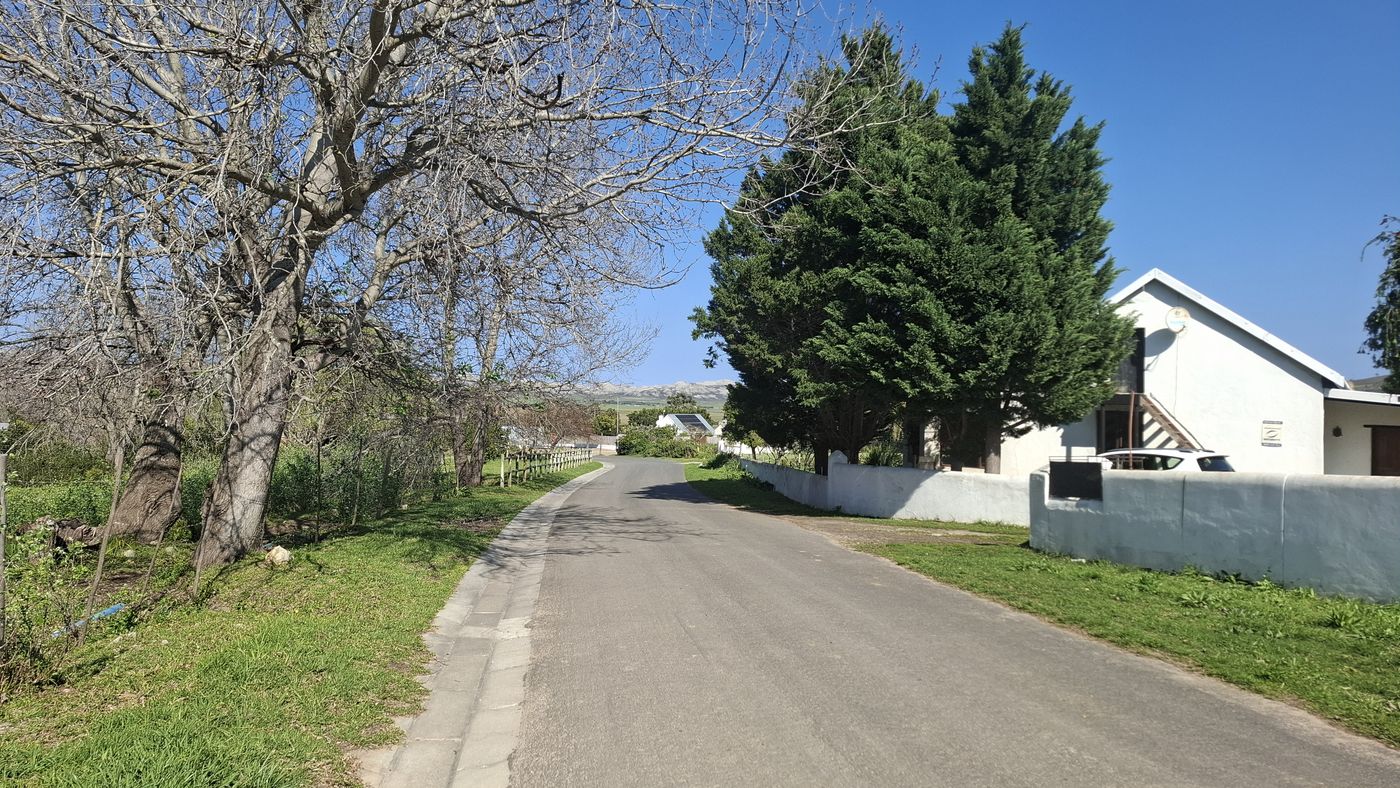 Die befestigte Straße am Grundstück vorbei, dahinter ein Nachbarhaus hinter einer weißen Mauer