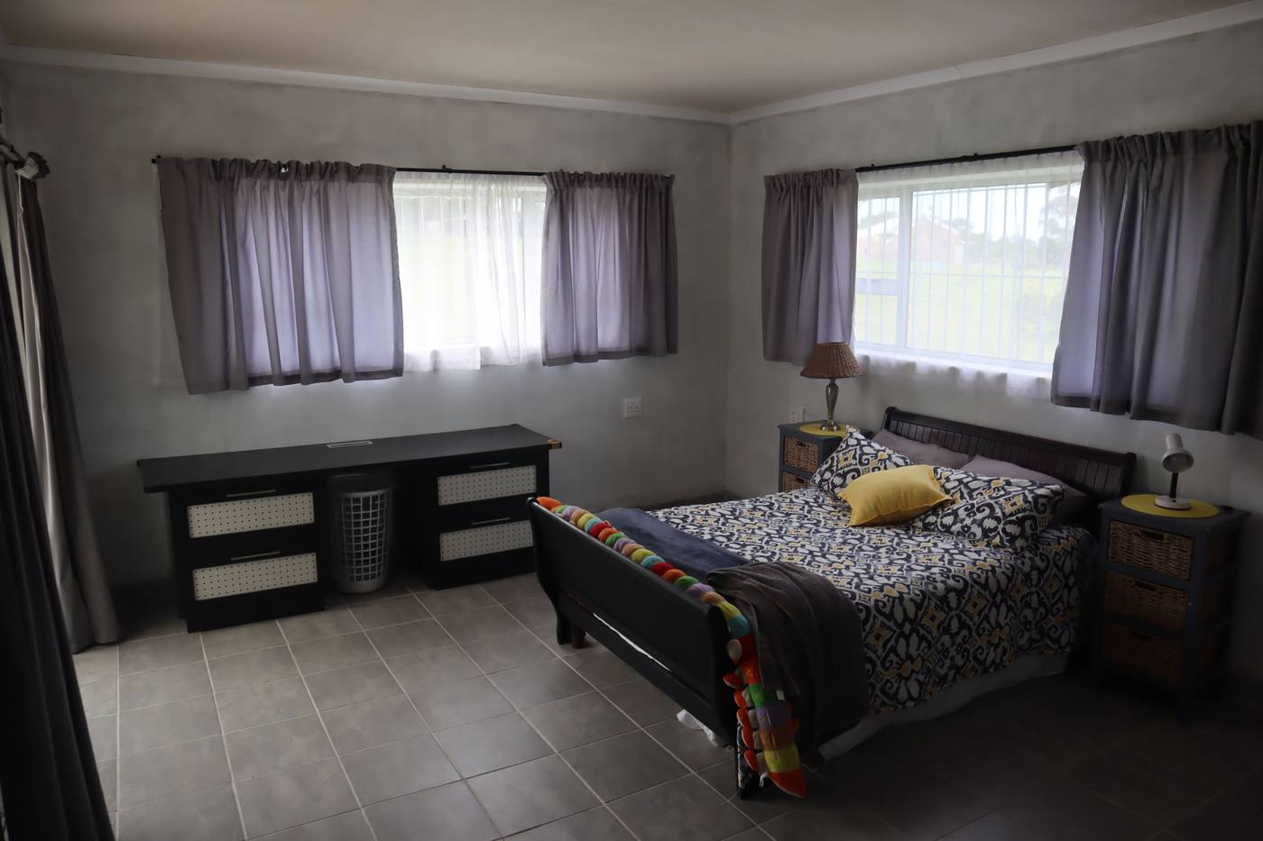 A large double bedroom with two windows and grey tiled floors