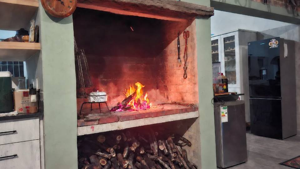 A fire going in the indoor braai, with wood stacked underneath