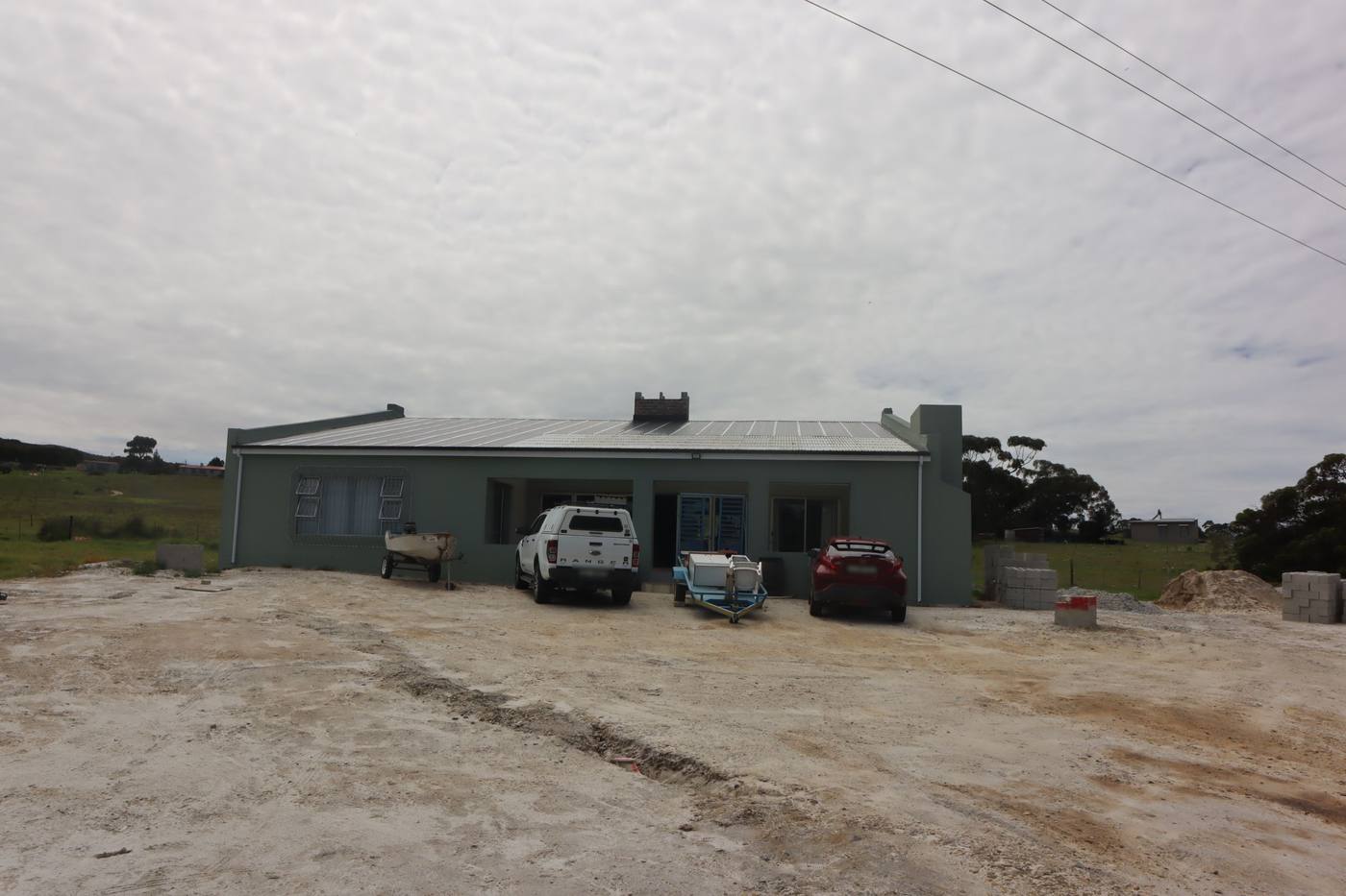 The front of the house across the gravel yard, with a covered stoep in the middle and vehicles parked outside