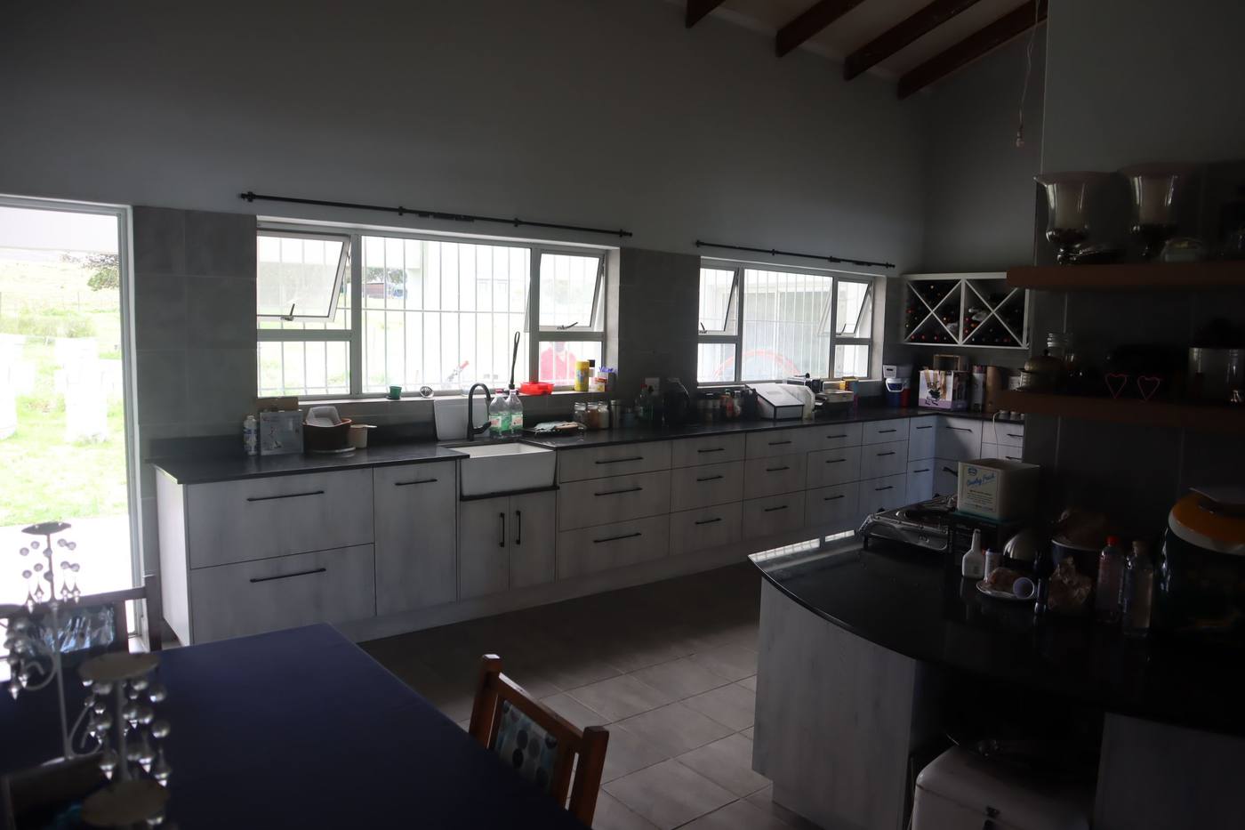 The open-plan kitchen: a long run of white cupboards under the windows, dark granite tops and a pitched ceiling