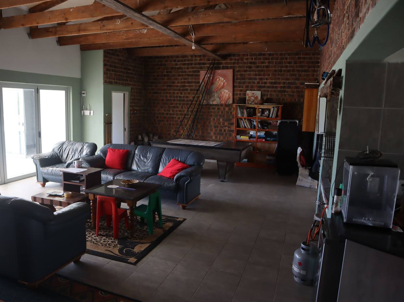 The open-plan living area under exposed timber beams and a face-brick wall, with sofas and room for a pool table