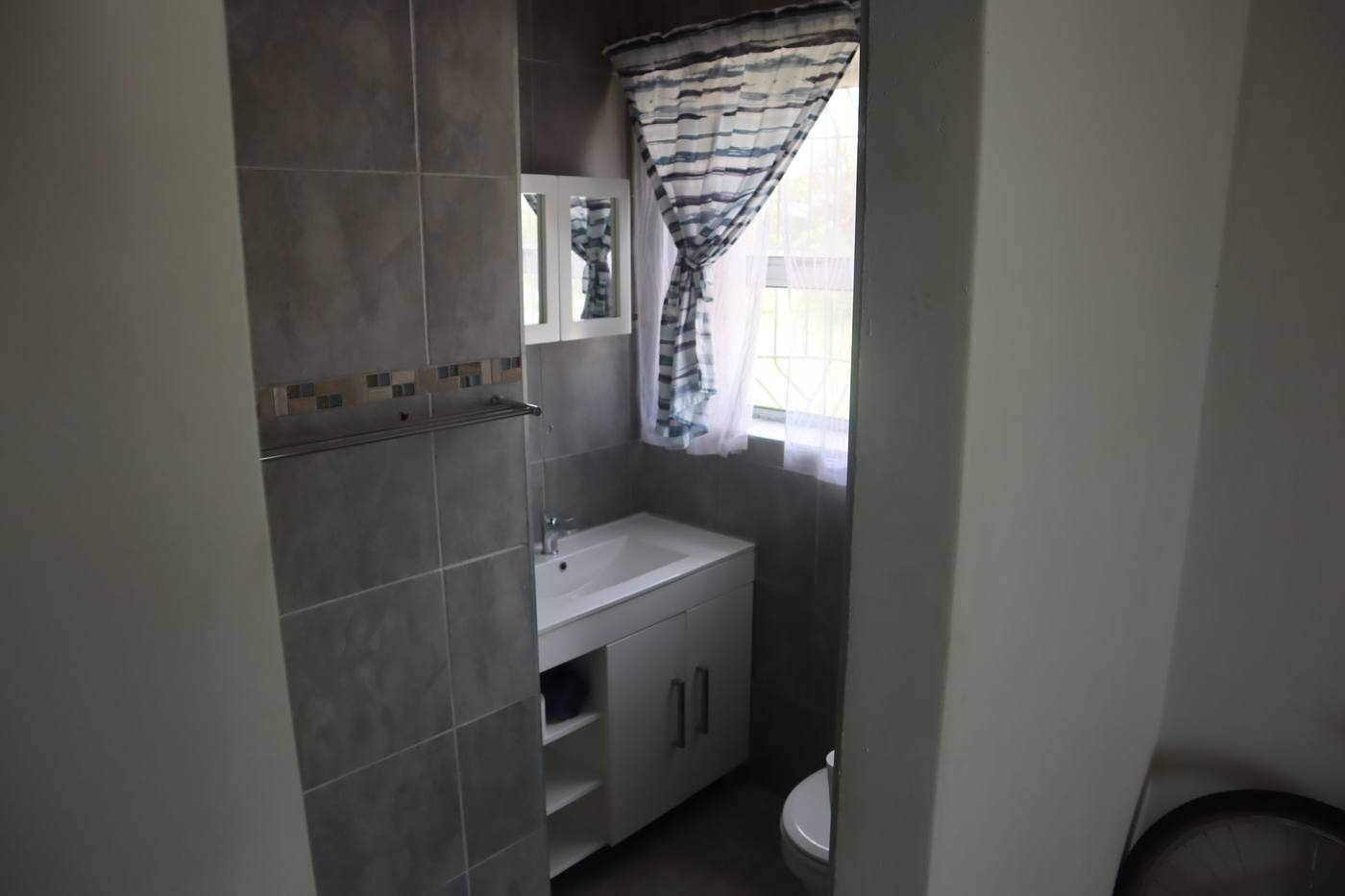 A basin and cupboard under a window in the same bathroom