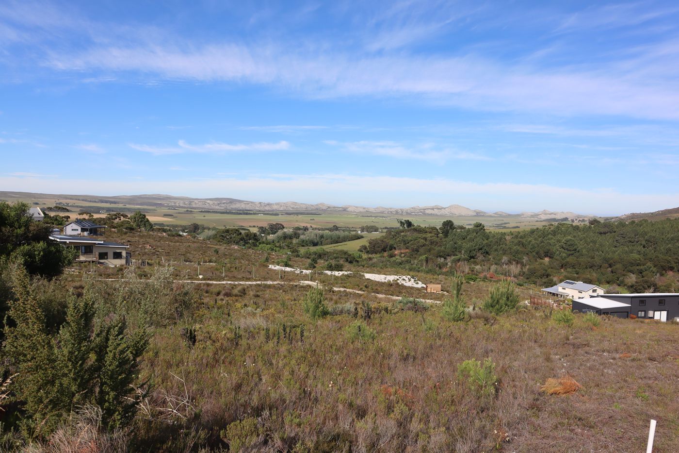 Fynbos on the upper slope falling away to the valley, with neighbouring houses on either side and farmland running out to the far hills