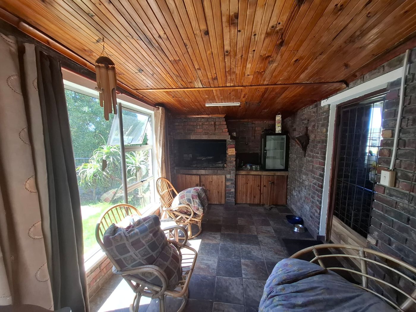 Der Braai-Raum mit eingebautem Grillplatz, Sichtziegelwänden und Holzdecke