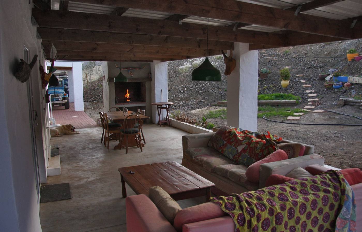 A covered back stoep with sofas, a dining table and a fireplace at the far end