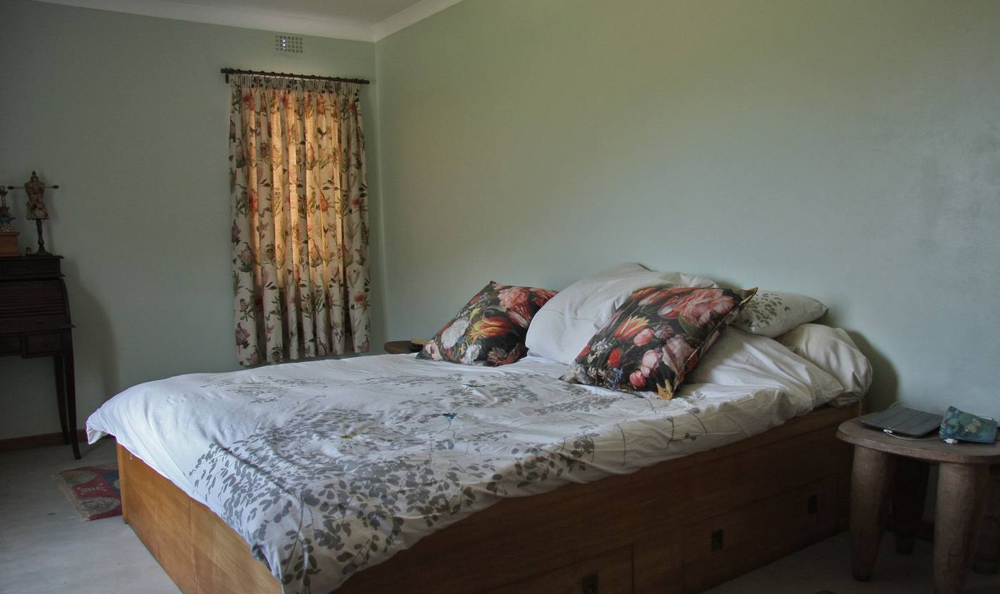 A bedroom with a wide bed, soft green walls and a curtained window