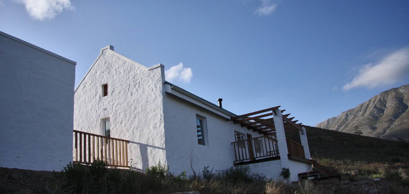 The mountain cottage from below: white walls, a steep gable and a timber deck