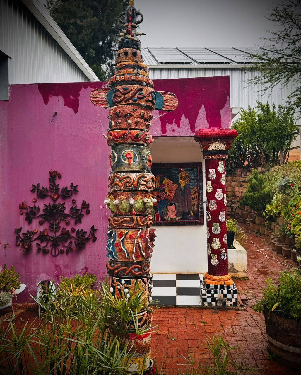 A brick-paved courtyard with a carved totem pole, a pink wall and potted plants