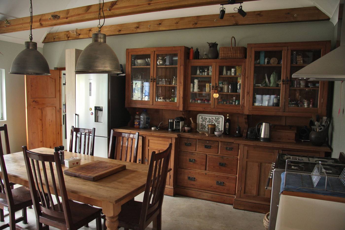 A dining room with a wooden table, timber dressers and pendant lights under a beamed ceiling