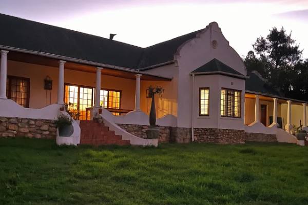 The farmhouse at dusk, lights on behind the verandah and the gable