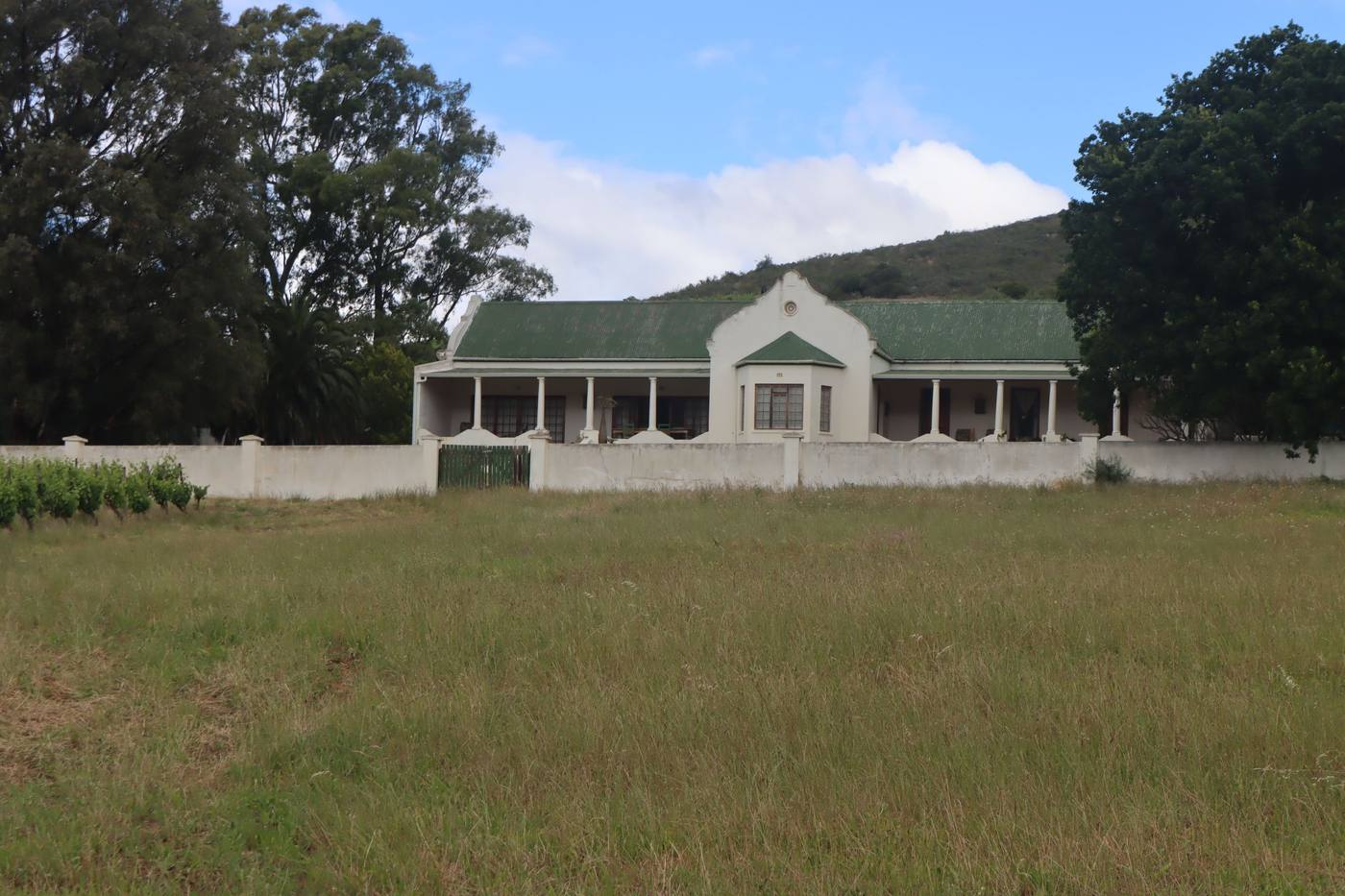 The farmhouse behind its white boundary wall, seen across an open field