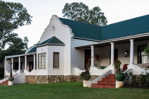 The farmhouse: a white Cape gable, a green roof and a long verandah on white columns, above a lawn