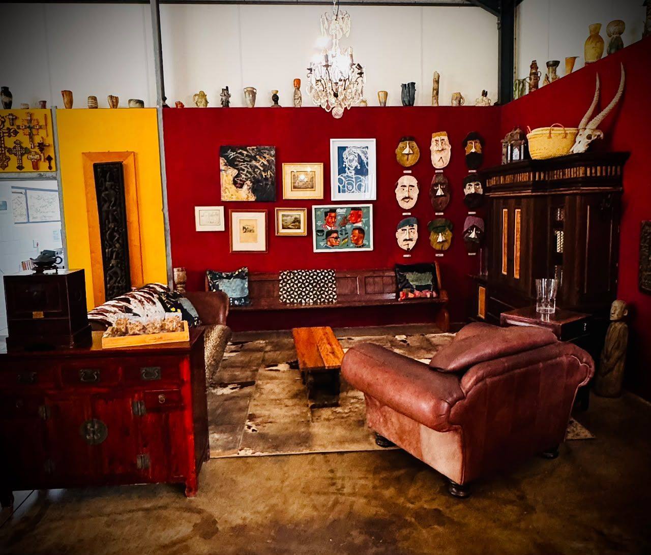 A high-ceilinged room with red walls hung with art and masks, leather sofas and a chandelier