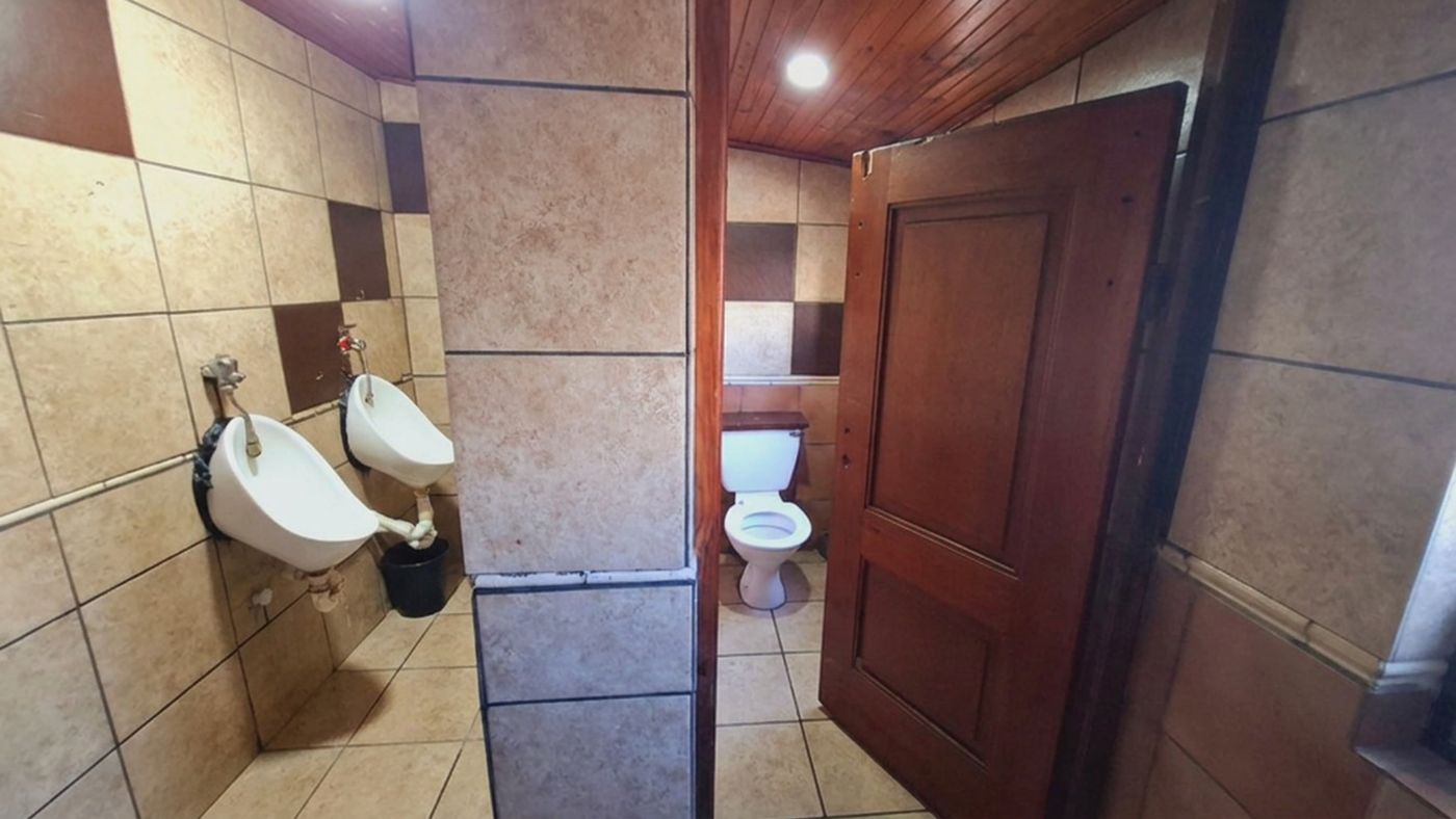 Die gefliesten Herrentoiletten mit zwei Urinalen und einer Kabine