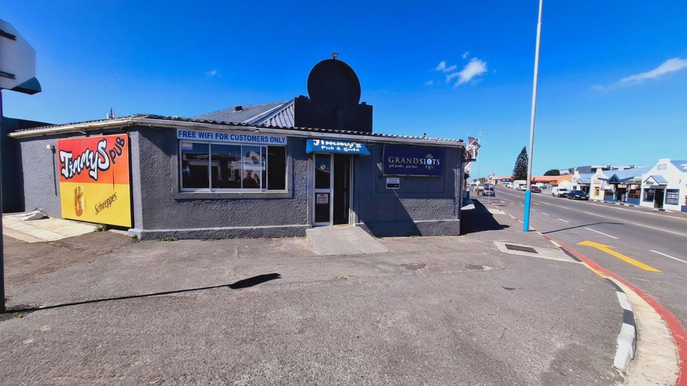 Der Pub an seiner Straßenecke: ein Jimmy's-Pub-Schild an der Seitenwand, das Schild des Pubs über der Tür und daneben das Grandslots-Schild, dahinter die Straße, die an den Geschäften des Ortes vorbeiführt