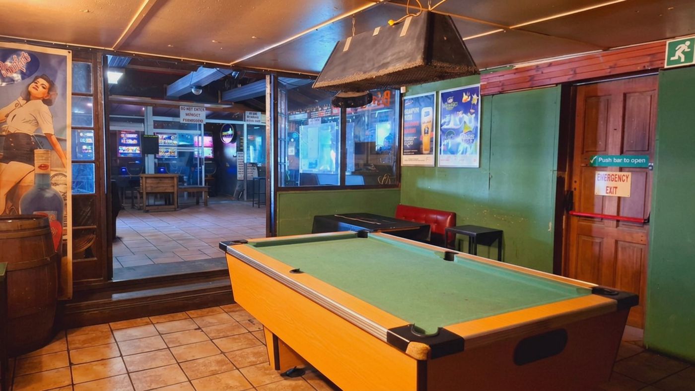 Ein Billardtisch im Spielraum, dahinter durch die Glasscheibe der Spielbereich