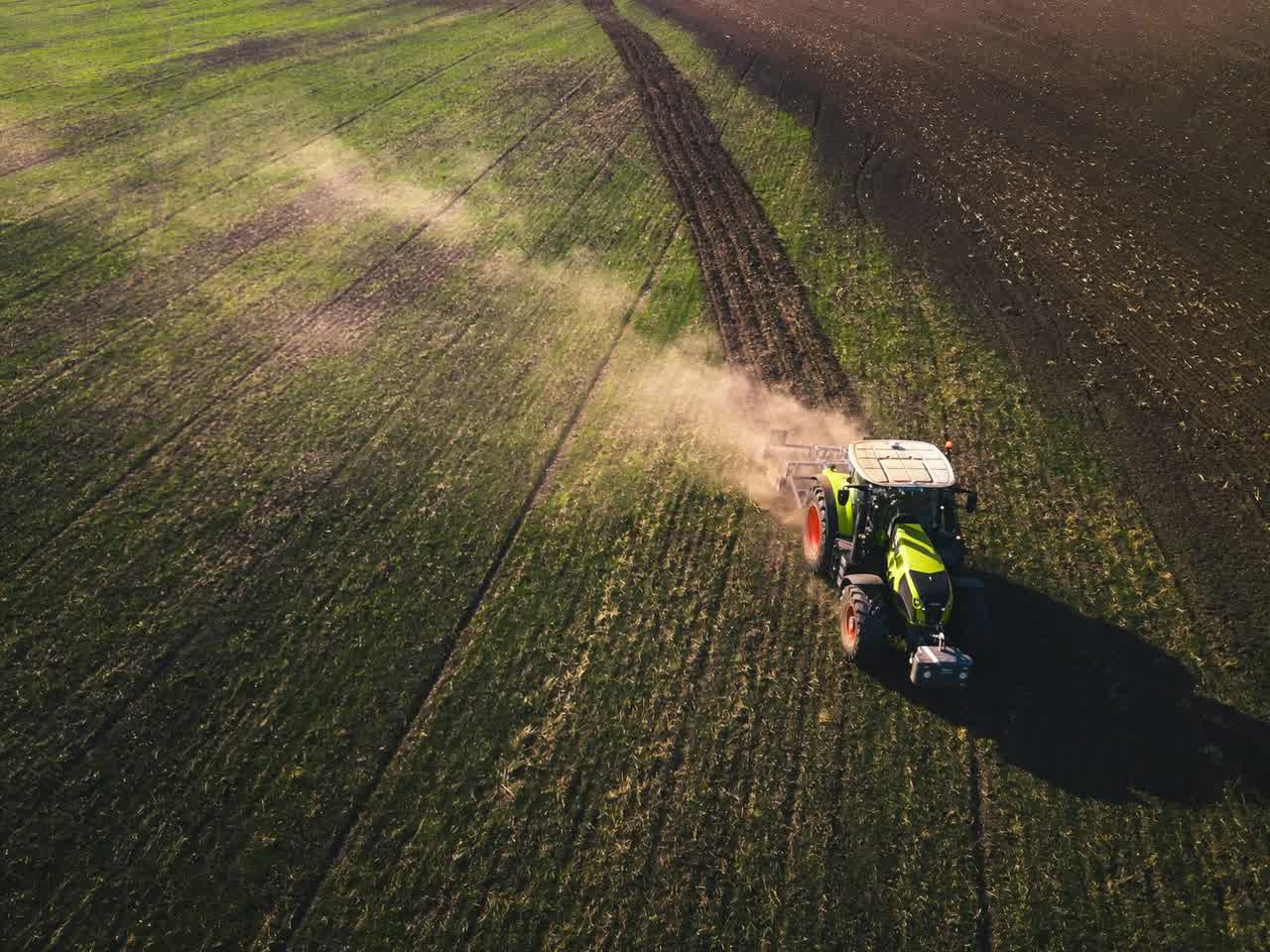 A tractor working a field from above, dust trailing behind the implement