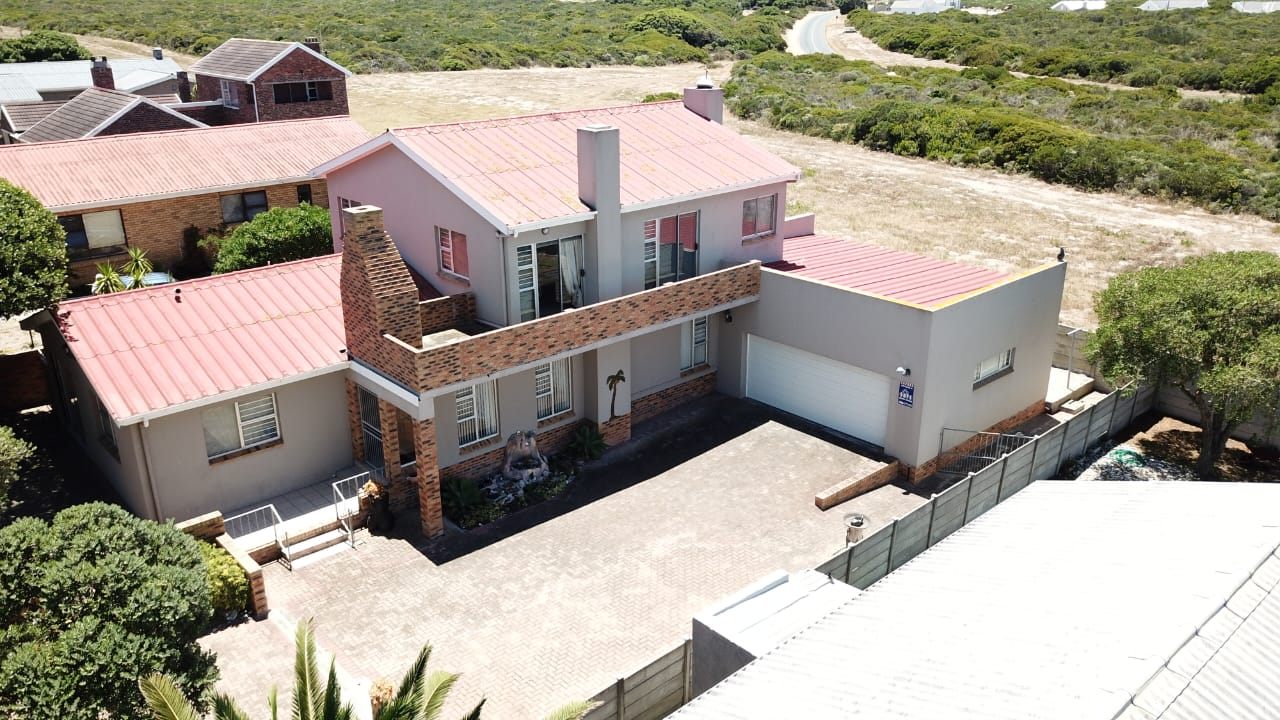 The house from above, its brick chimney and balcony over the paved driveway, the double garage beside it and fynbos behind