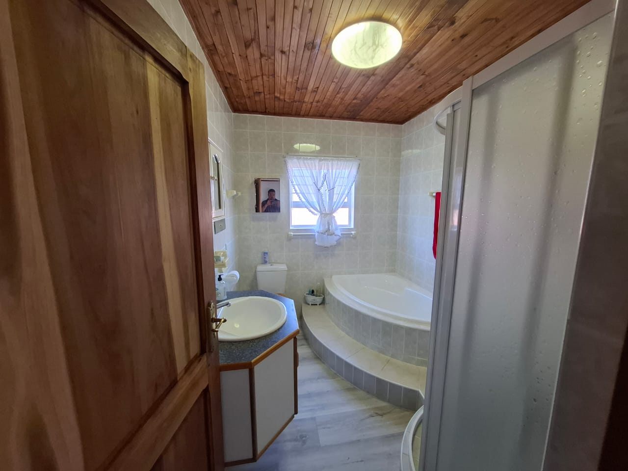 The bathroom: a corner bath, a basin and a frosted window under a pine ceiling