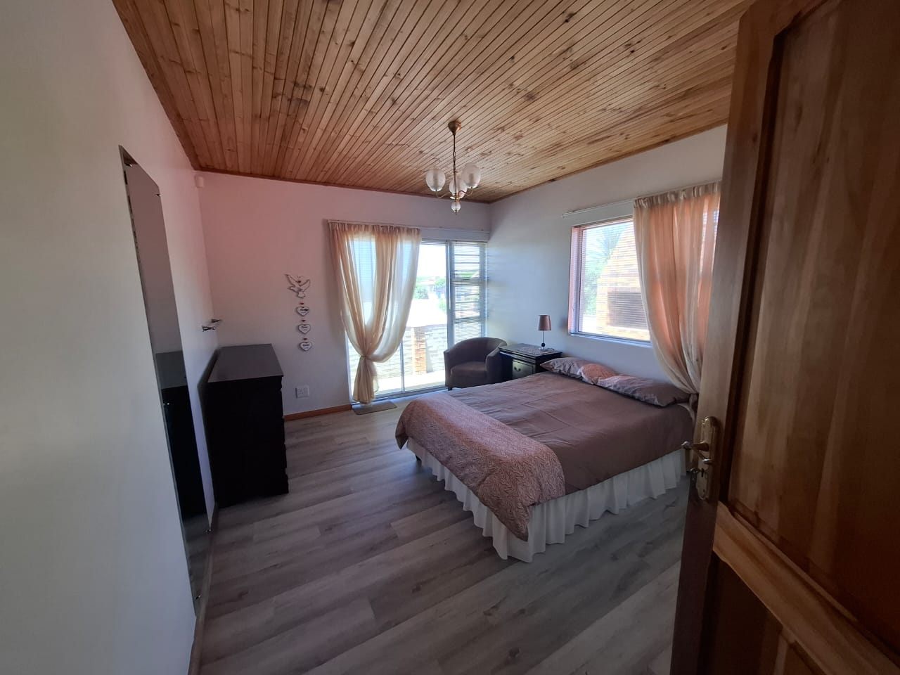 A bedroom with a pine ceiling, a double bed and a window with curtains