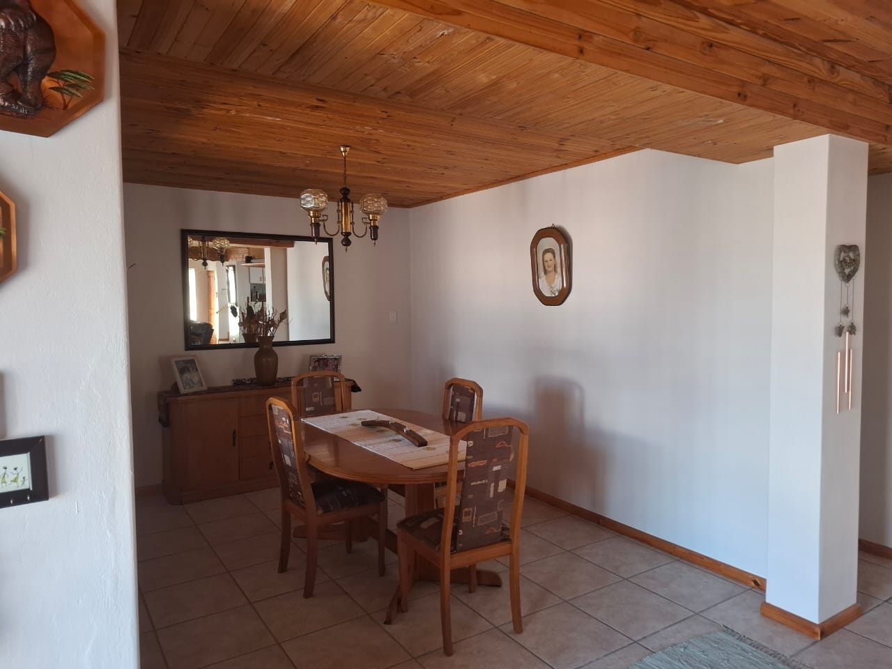A dining table and chairs in a tiled corner, with a mirror and sideboard against the wall