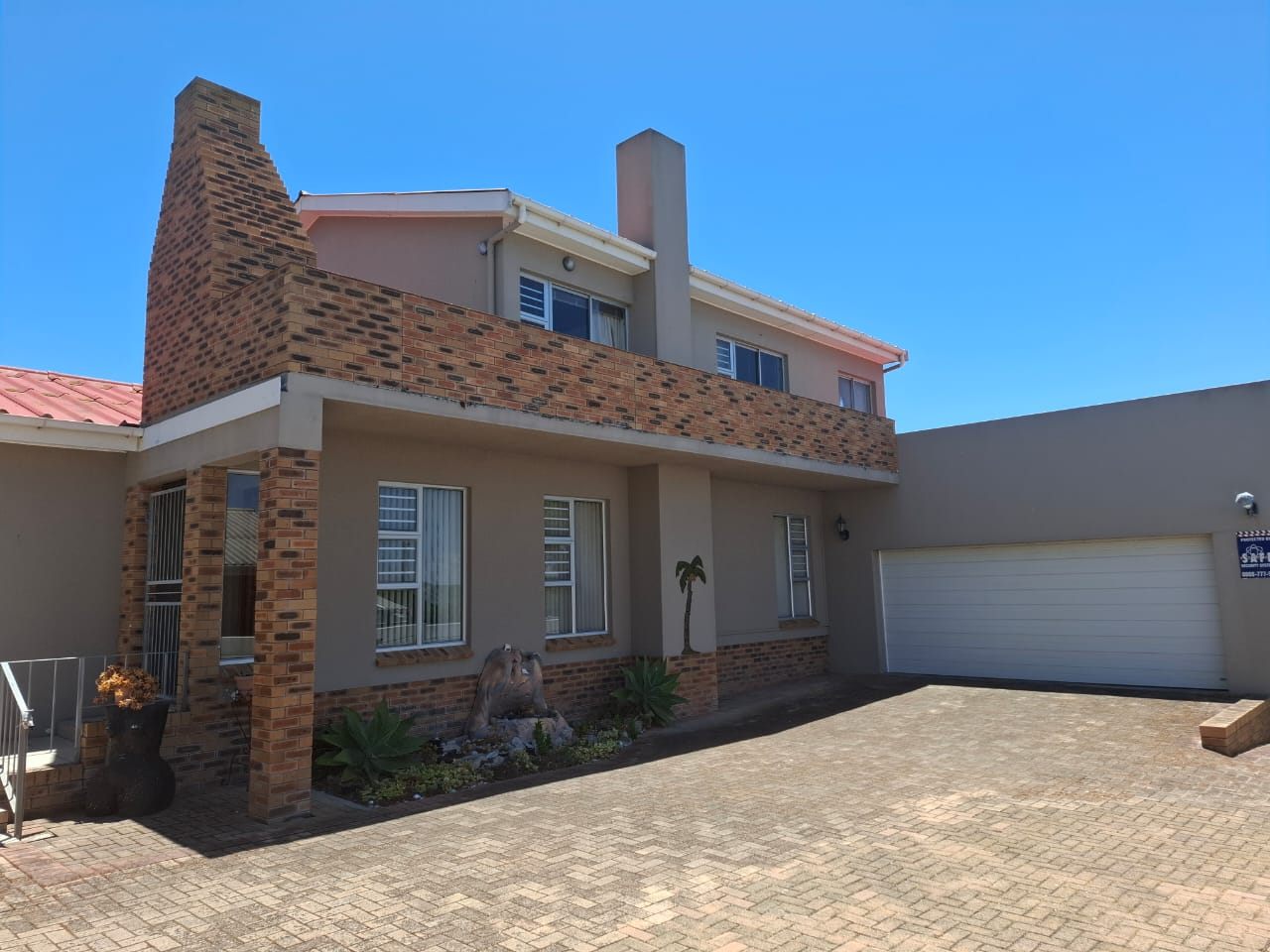 The brick-paved driveway in front of the house, with the white double garage door on the right