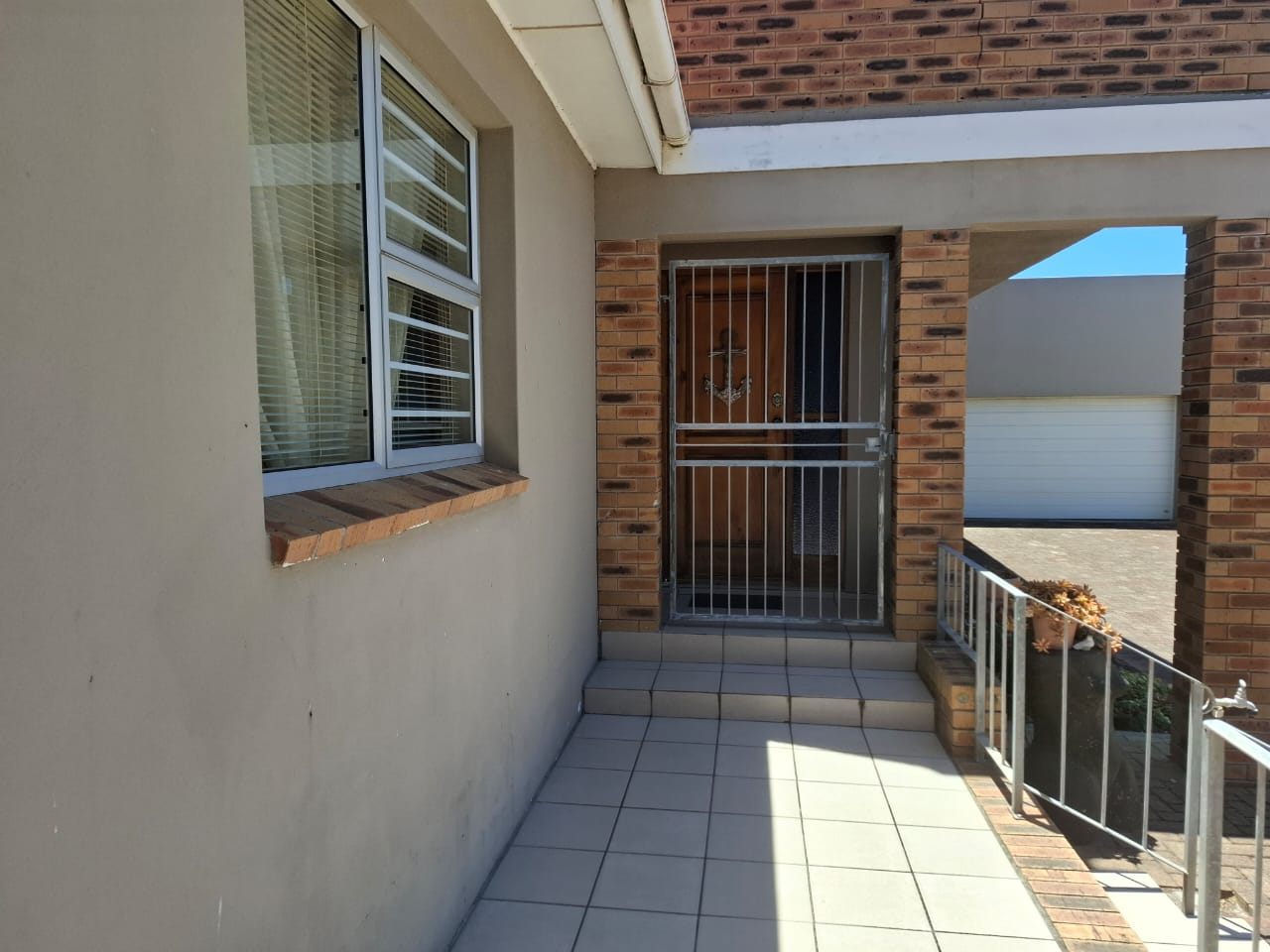 A tiled walkway to the front door behind its security gate, under a brick pillar