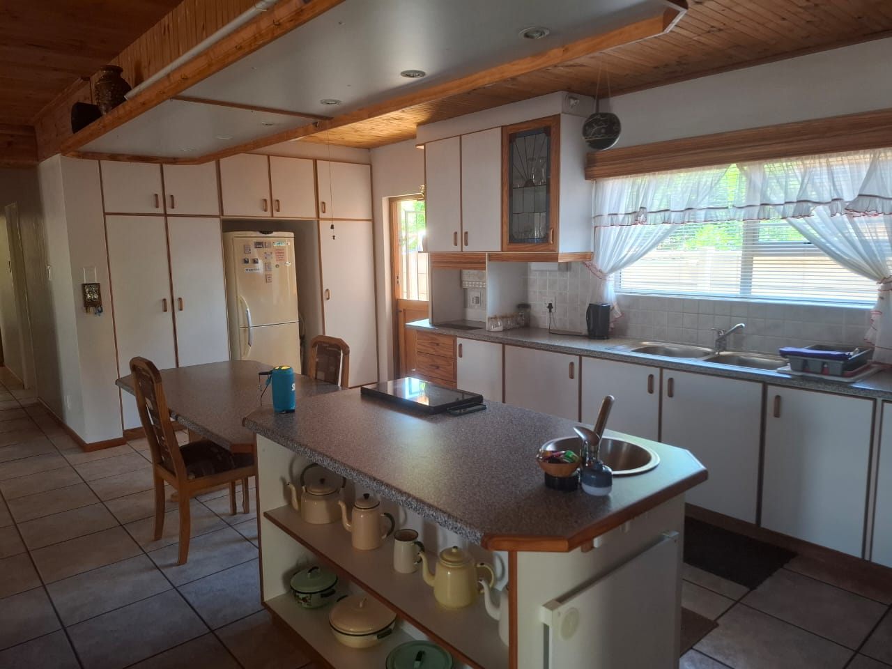 The kitchen island with a vegetable basin, white cupboards behind and a tiled floor