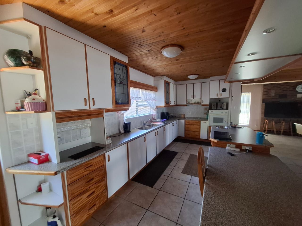 The kitchen counter and cupboards running through to the living area, under a pine ceiling
