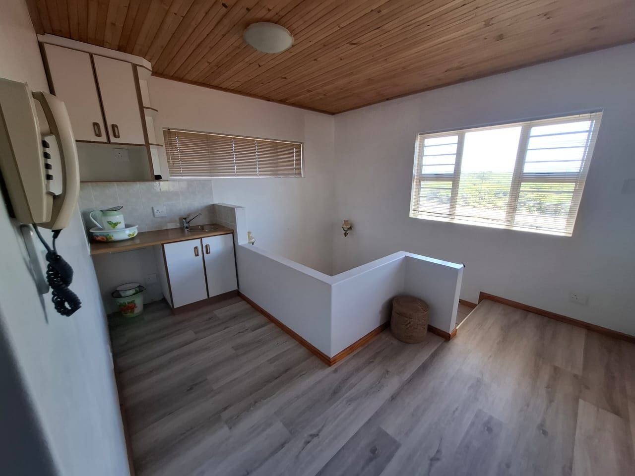 A small kitchenette with a counter and cupboards at the top of the stairs, on a wood-look floor