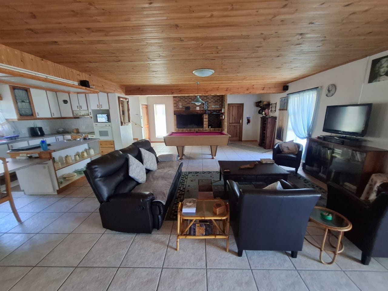 The open-plan living room: leather couches, a pool table and the brick braai at the back, under a knotty-pine ceiling