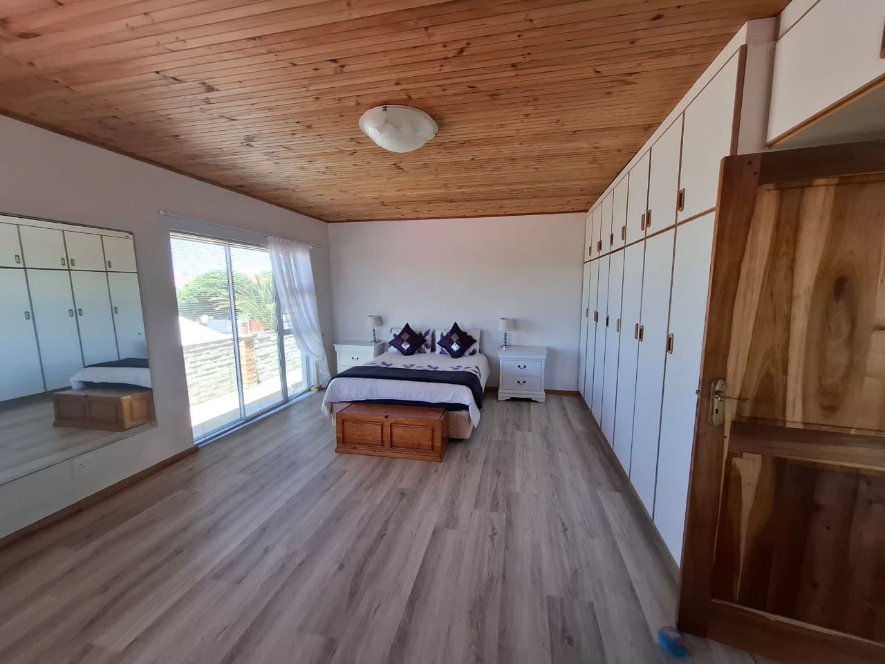 A large bedroom with a wood-look floor, a wall of built-in cupboards and sliding doors to the balcony