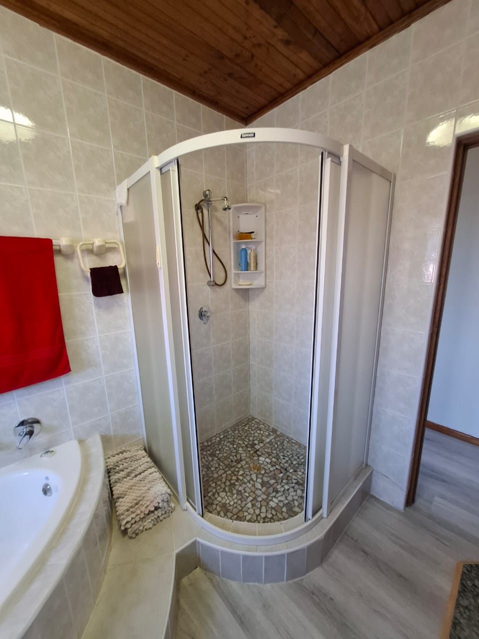 A corner shower cubicle in a tiled bathroom, with the bath beside it