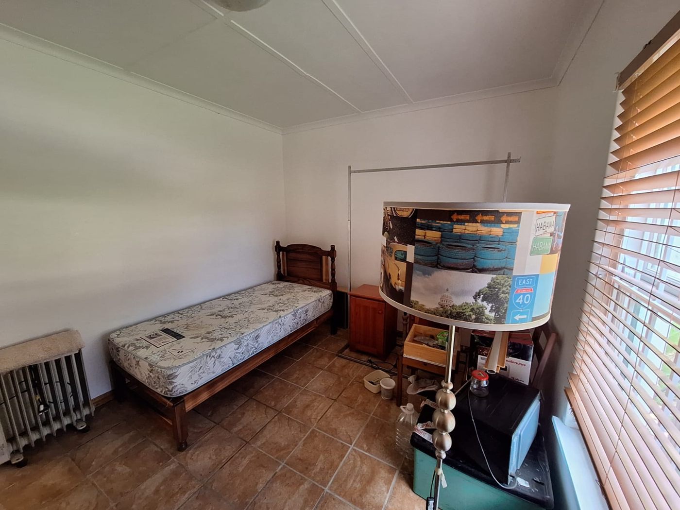 A small bedroom with a single bed, a wooden floor and blinds