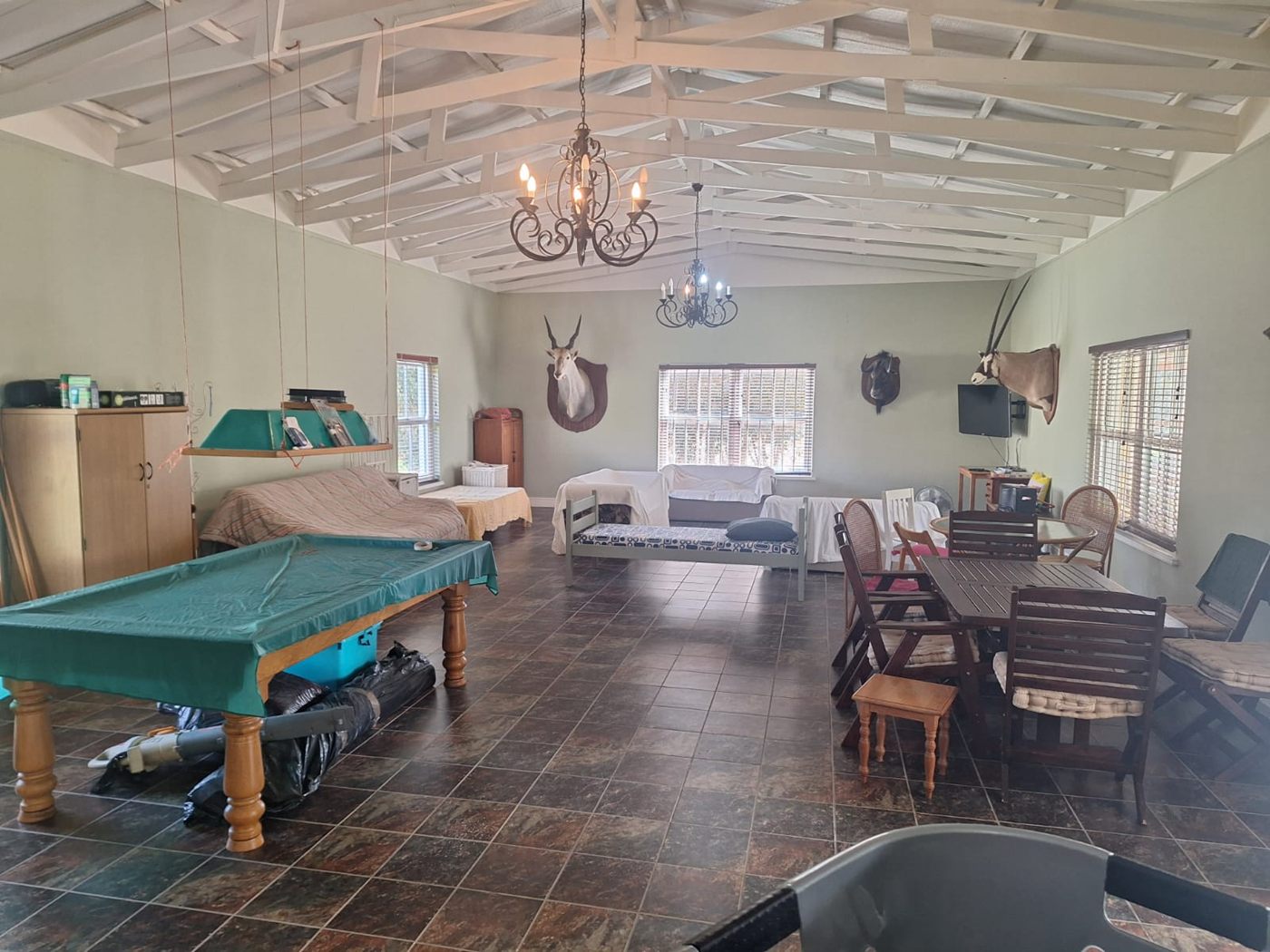 The entertainment room under a white timber ceiling, with a pool table, a dining table and chandeliers