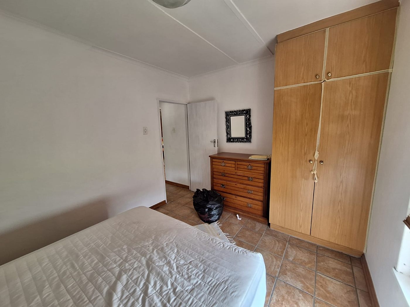 A cottage bedroom with a built-in wooden cupboard and a chest of drawers
