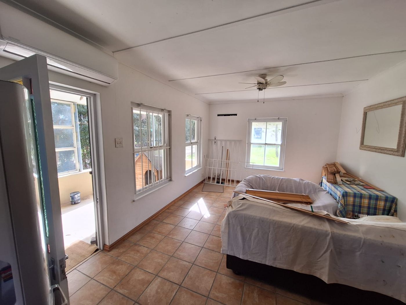 A bedroom with a tiled floor, a ceiling fan and a door to the stoep