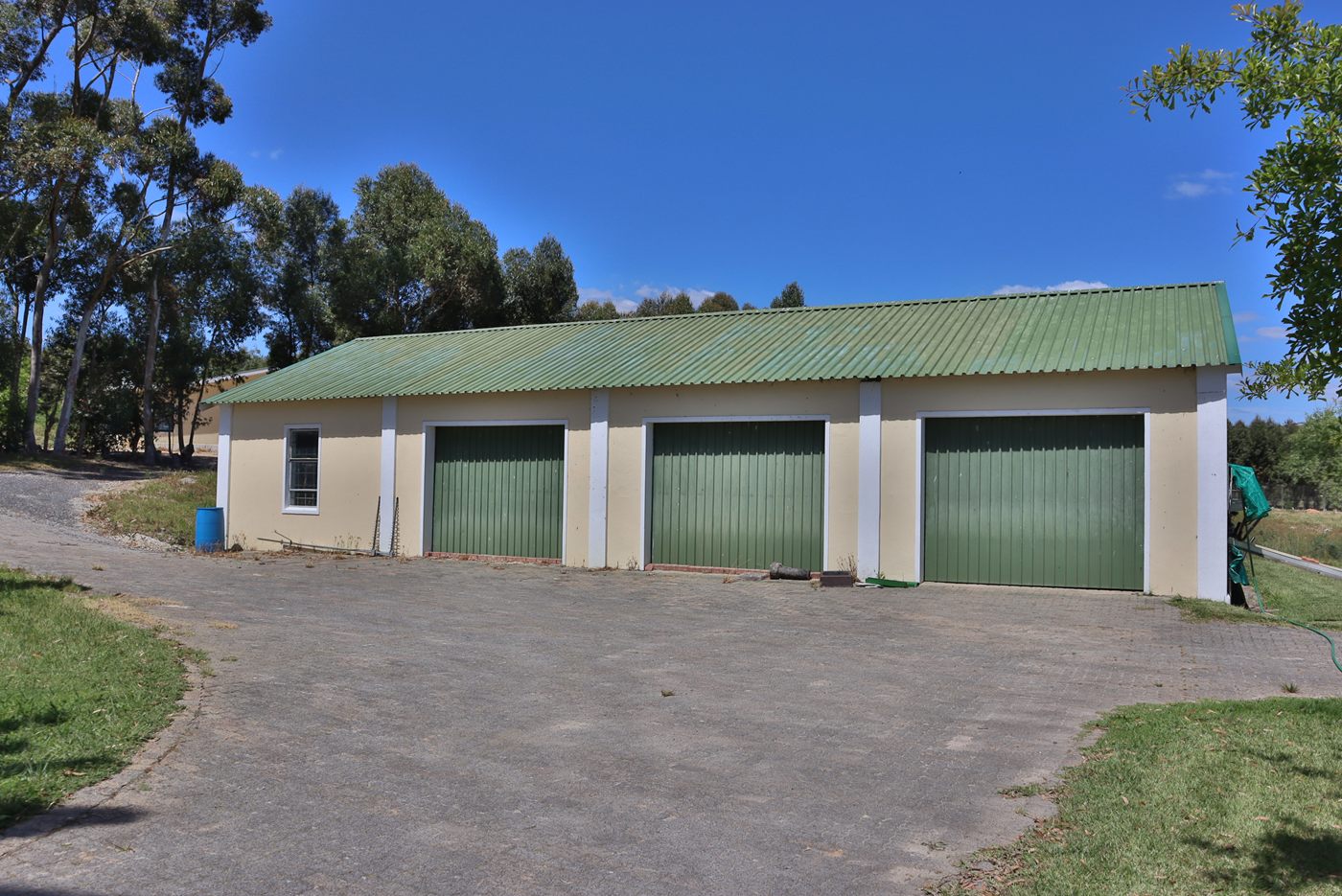 The garage block: three green doors under a green roof, with a paved yard in front
