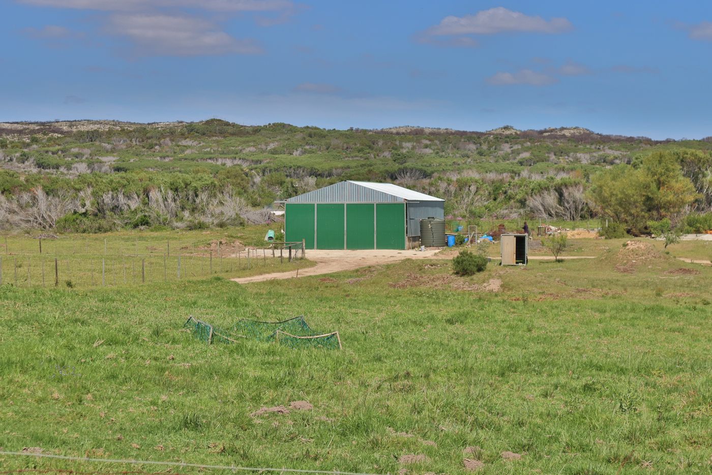 A green steel shed in an open camp, with fynbos hills behind