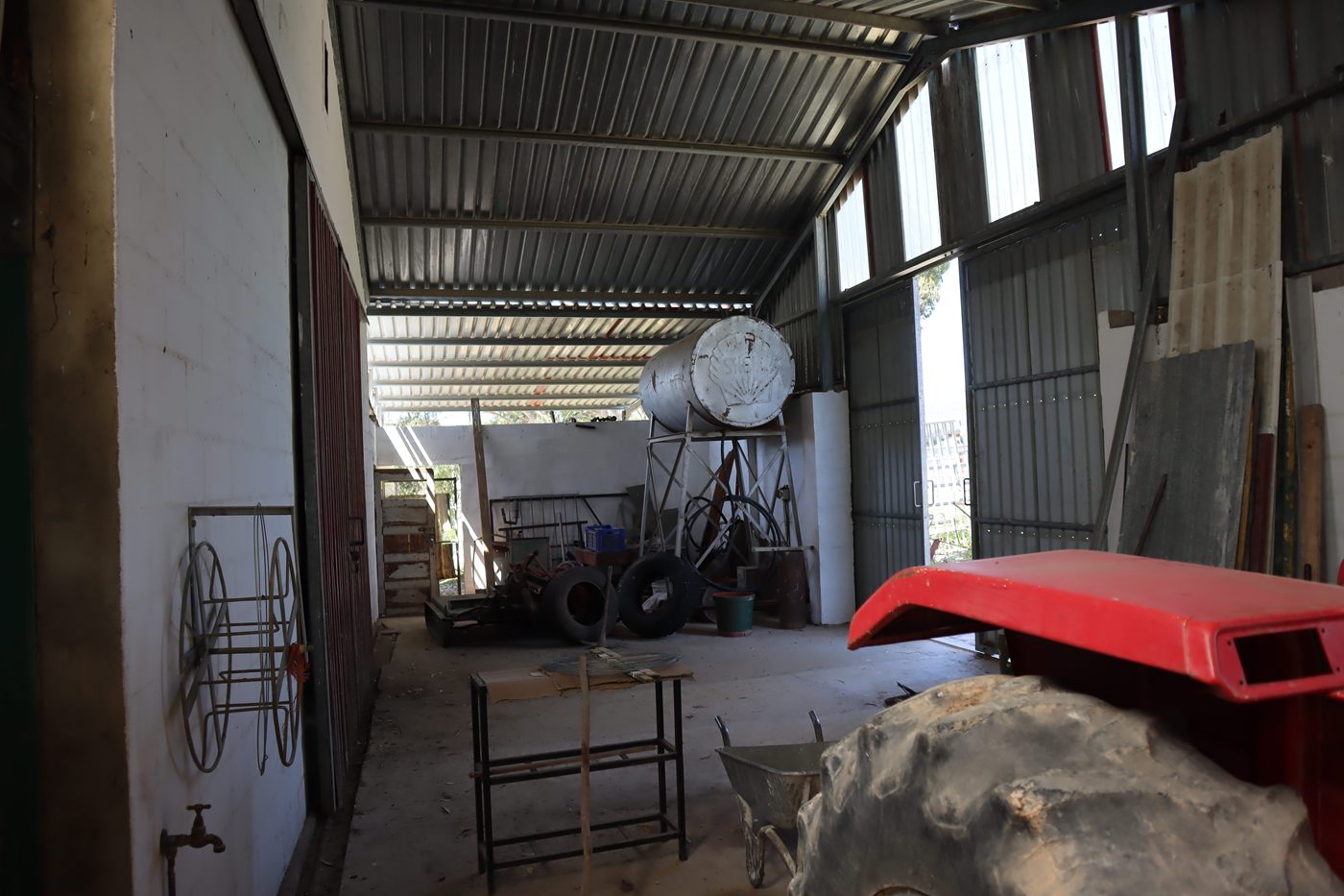 Inside a long shed, with tools along the wall and a red tractor bonnet in front