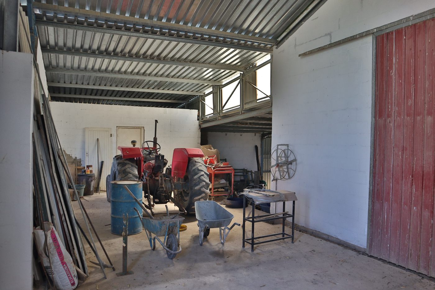 Inside a shed: a red tractor, a wheelbarrow and tools