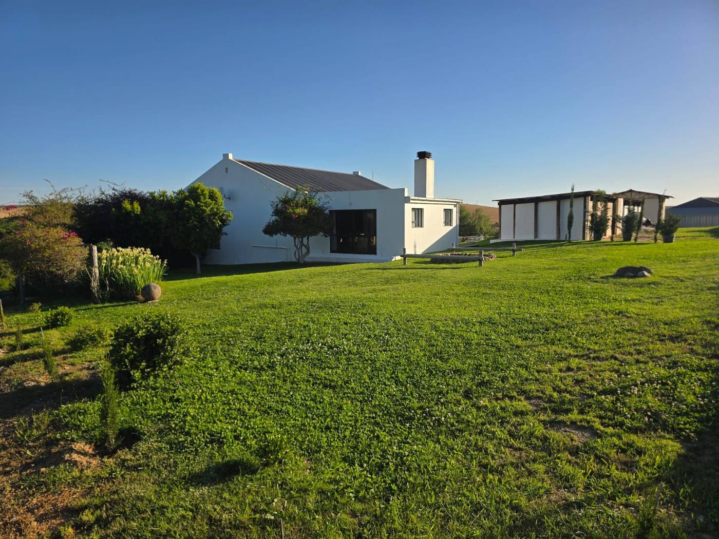 A white house with a chimney on a wide lawn, with a covered outdoor room to the right
