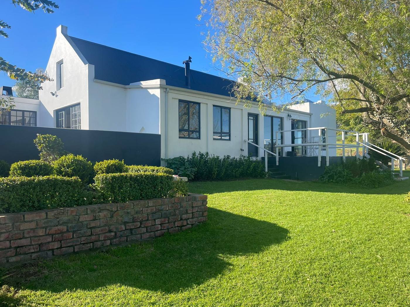 The main house: white walls, a dark roof and a gable, above a lawn edged with a low brick wall