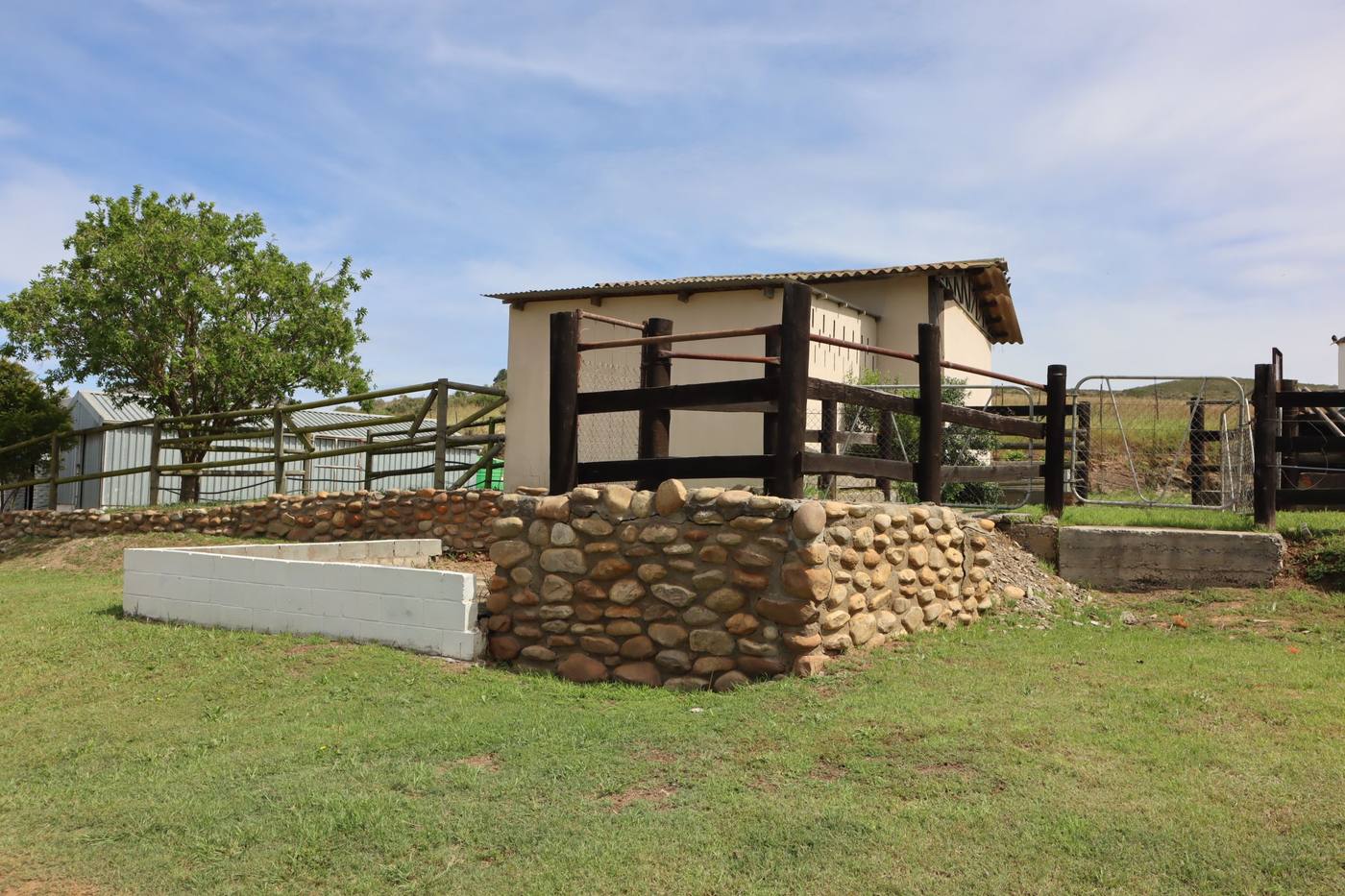 A pen with timber rails and a stone-packed loading ramp, beside a small outbuilding