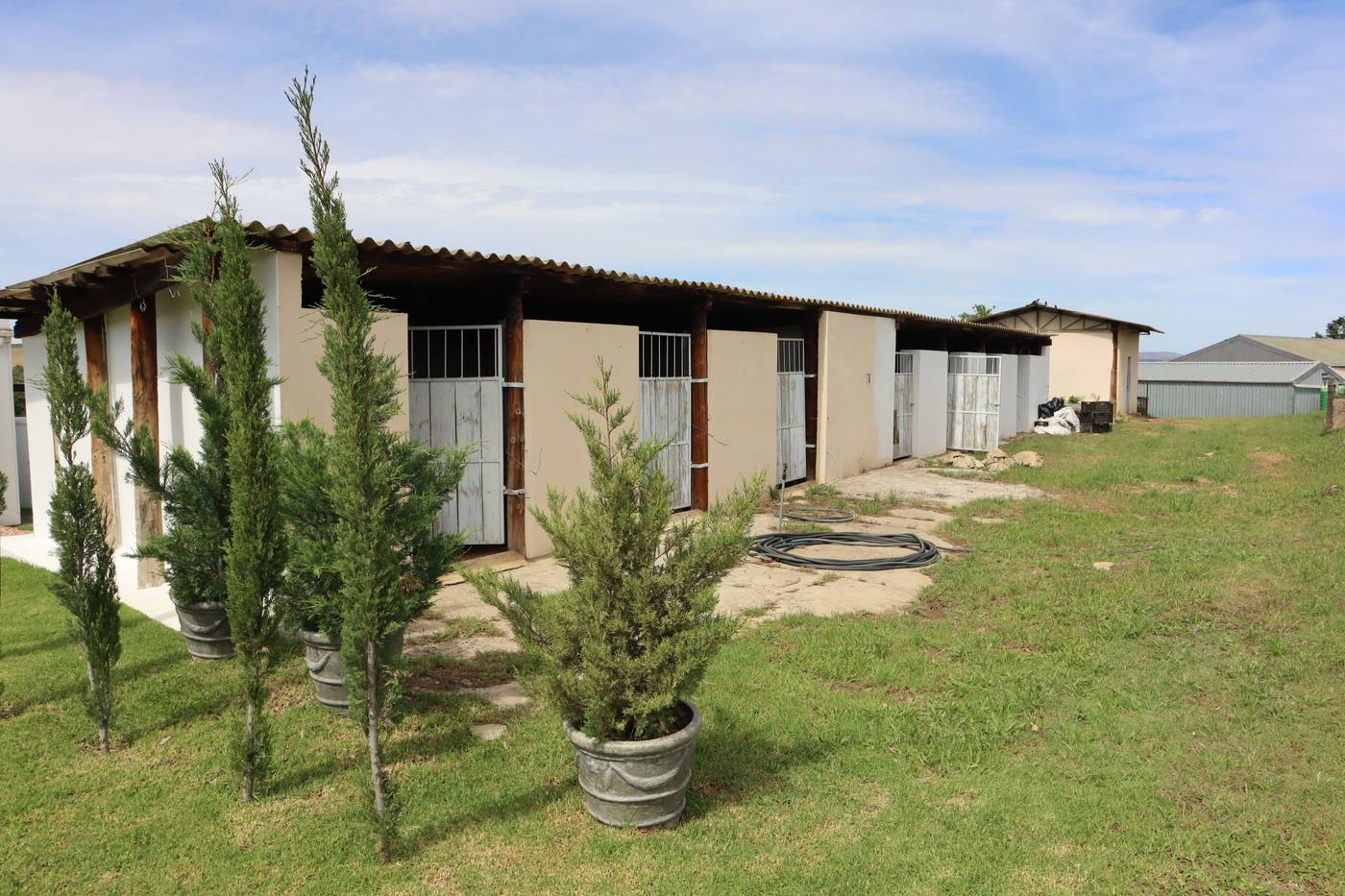 The horse stables: a row of stalls under a timber-posted veranda, with young cypress trees in front
