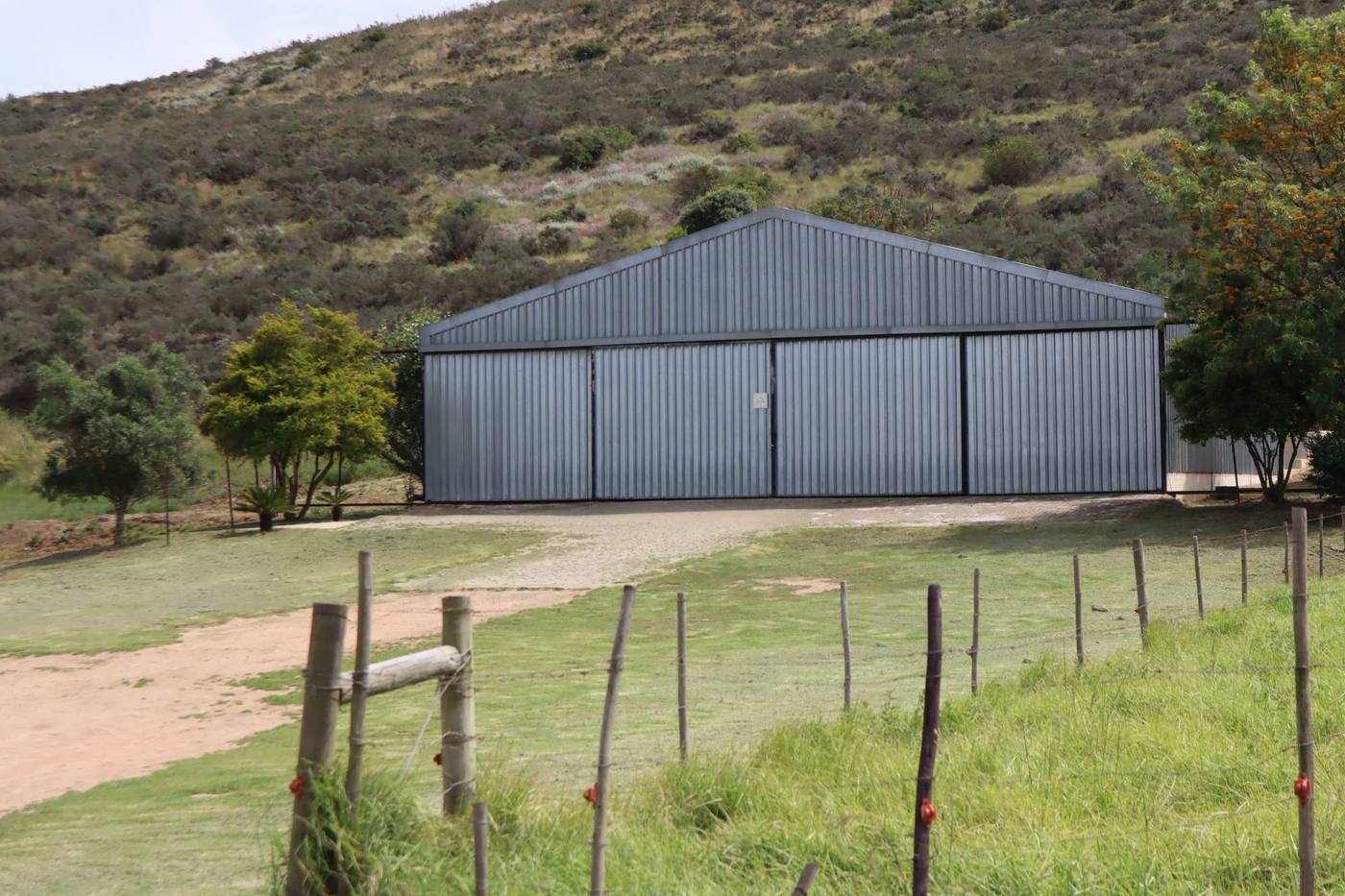 A second steel shed, its doors closed, under a fynbos hill