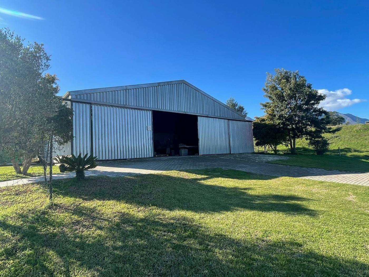 A steel shed with its doors open, on a lawn among trees