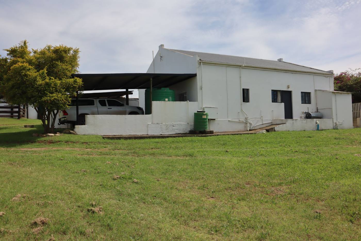 A long white farm building with a carport and water tanks beside it, on a wide lawn